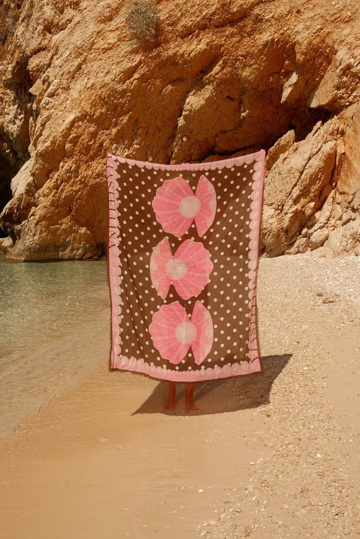 Lola pareo in Shell & Pearl Polka Dot held open on a sandy beach, showing the full shell and pearl print with pink border